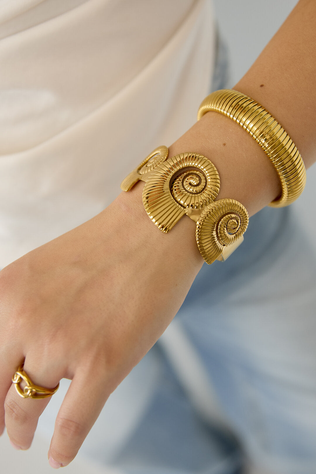 Pulsera tipo brazalete con diseño de conchas en espiral.