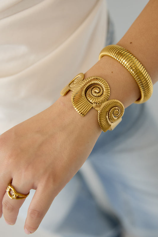 Pulsera tipo brazalete con diseño de conchas en espiral.